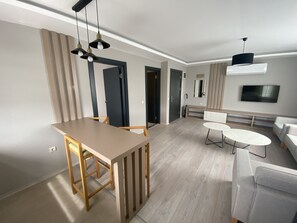 A modern living room with a dining area, a sofa, a TV, and a ceiling light fixture. - Via Suite (Antalya)