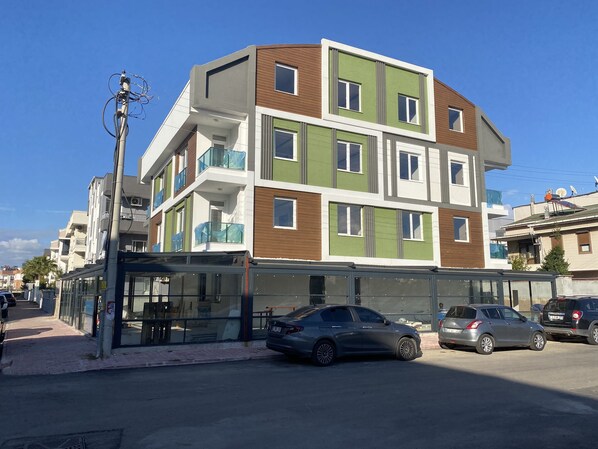 A multi-story residential building with balconies, a glass storefront, and parked cars. - Via Suite (Antalya)