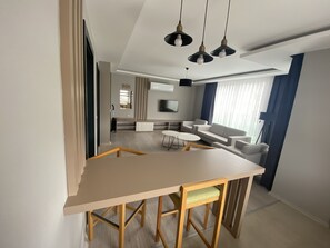 A modern kitchen with a central island, a dining area with a table and chairs, and a living area with sofas and a TV. - Via Suite (Antalya)