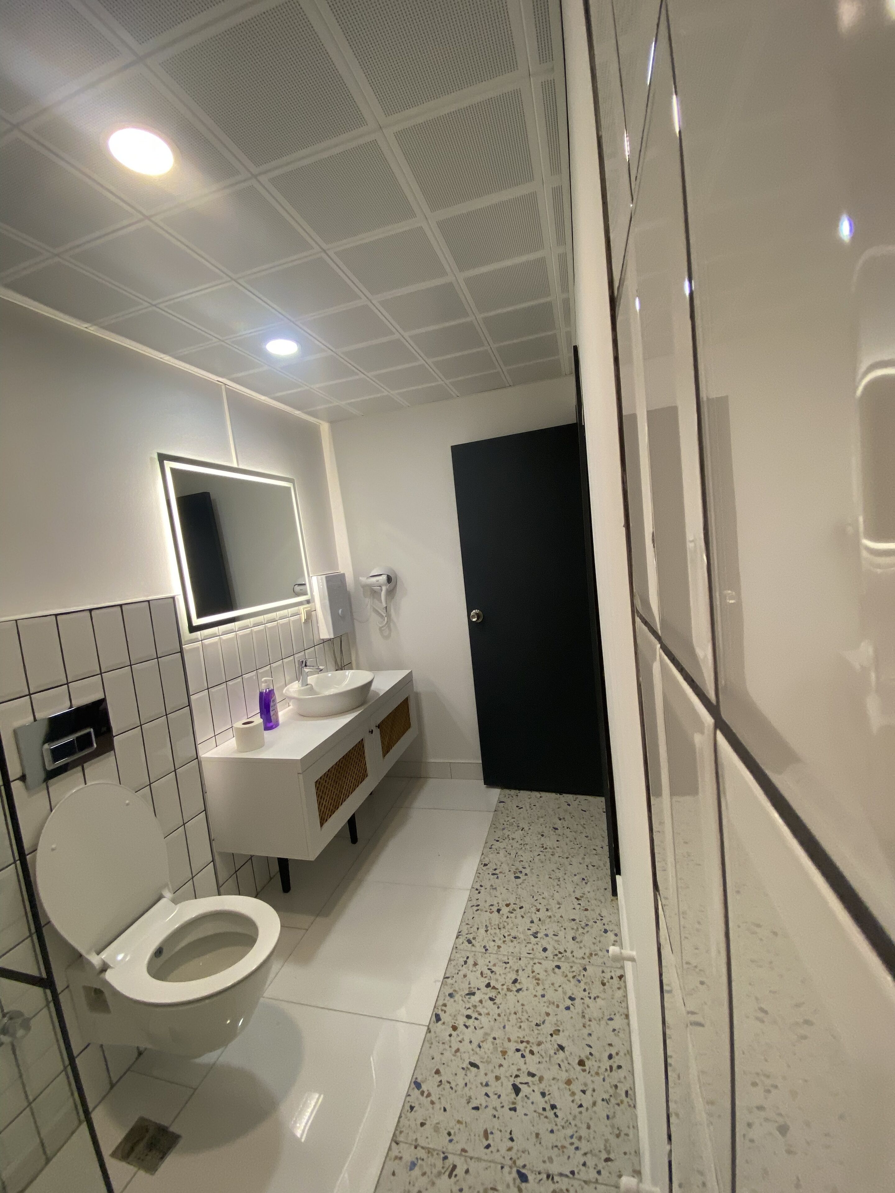 A modern bathroom with a toilet, sink, mirror, and a black door.