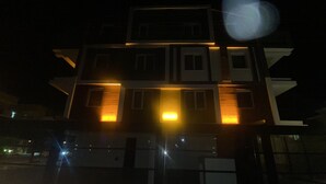 Un immeuble à plusieurs étages, doté de fenêtres illuminées et d’une entrée au rez-de-chaussée bien visible.