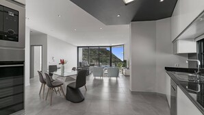 A modern kitchen with a dining area, large windows, and a view of the outdoors. - Villa Calheta Charm by Villa Plus (Arco Da Calheta)