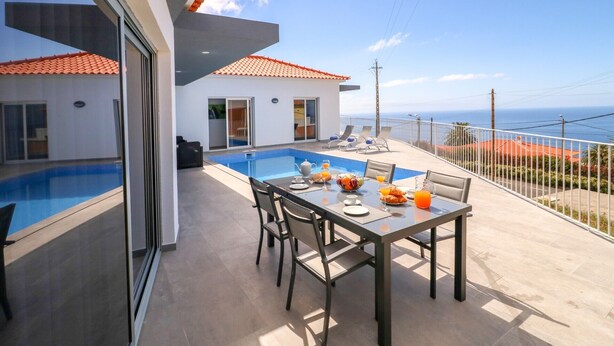 Un balcón con piscina, mesa y sillas, con vistas a la costa.