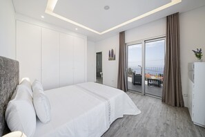 A modern hotel room with a large bed, a wardrobe, a bathroom, and a balcony with a view.
