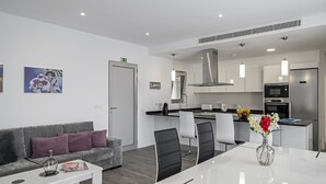 Un apartamento moderno con sala de estar que incluye un sofá gris, una mesa de comedor con sillas y una cocina con electrodomésticos de acero inoxidable.