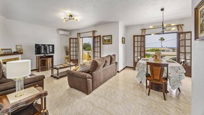 A living room with a sofa, TV, and dining area with a table and chairs. - Villa Campos by Villa Plus (Guia)