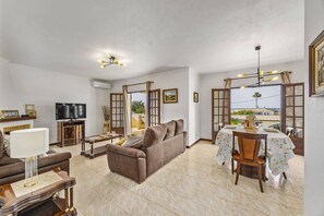 A living room with a sofa, TV, and dining area with a table and chairs. - Villa Campos by Villa Plus (Guia)