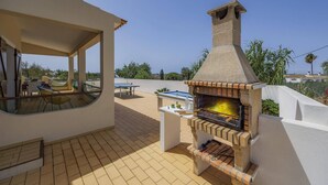 An outdoor patio with a brick oven, seating area, and a view of the landscape. - Villa Campos by Villa Plus (Guia)
