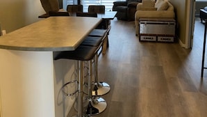 A modern kitchen with a bar area, a dining table with chairs, a sofa, and a large window with blinds. - Most Equipped! - Condo le mieux équipé - Orford QC (Orford)
