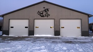 A large industrial building with three garage doors and a logo above the central door. - Outdoorsman Paradise- 1/2 mile from Lake Oahe (Pierre)