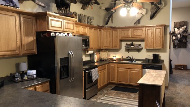 A kitchen with wooden cabinets, a stainless steel refrigerator, a microwave, and a ceiling fan. - Outdoorsman Paradise- 1/2 mile from Lake Oahe (Pierre)