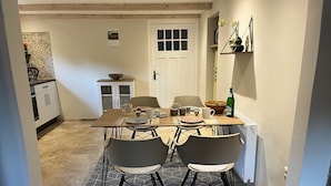 A dining area with a wooden table set for four, surrounded by modern chairs. A kitchen with cabinets and a sink is visible in the background. - Fehnhaus - cozy vacation apartment with house character (Großefehn)