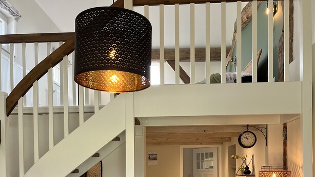 A spacious living area with a staircase, a dining table, and a sofa. - Fehnhaus - cozy vacation apartment with house character (Großefehn)