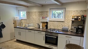 A modern kitchen with a gas stove, oven, and a coffee maker. - Fehnhaus - cozy vacation apartment with house character (Großefehn)