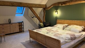 A bedroom with a sloped ceiling, a bed with a patterned bedspread, a wooden dresser, and a small window. - Fehnhaus - cozy vacation apartment with house character (Großefehn)