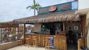 A beachside bar with a thatched roof, wooden stools, and a sign for Golden Drinks. - Golden Lake Residence (Arraial do Cabo)