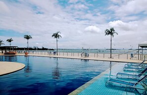 Une piscine avec des chaises longues, des palmiers et une plage en arrière-plan.
