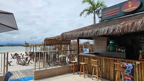A beachside bar with wooden chairs and tables, a thatched roof, and a view of the sea. - Golden Lake Residence (Arraial do Cabo)