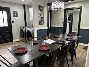 A dining area with a long table set for six, surrounded by chairs. There are two wall-mounted washing machines in the background. - "Mt. Holly Haven" — Near Whitewater Center, Belmont Abbey, Catawba River, CLT (Mount Holly)