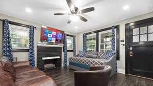 A living room with a fireplace, a ceiling fan, and a television mounted on the wall. - "Mt. Holly Haven" — Near Whitewater Center, Belmont Abbey, Catawba River, CLT (Mount Holly)