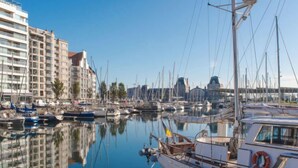 Ein Yachthafen mit vertäuten Booten, ein mehrstöckiges Gebäude und ein klarer, blauer Himmel.