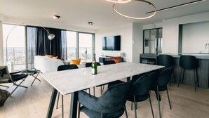 Ein modernes Hotelzimmer mit großem Esstisch, schwarzen Stühlen, Fernseher und Blick auf die Stadt.