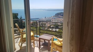 Un balcó amb mobles de vimet i taula, amb vista a una ciutat costanera amb edificis i una extensió d'aigua.