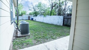 Ein Garten mit weißem Zaun, einer großen Klimaanlage und einer Rasenfläche.