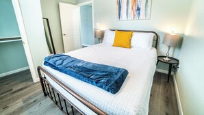 Ein ordentlich bezogenes Bett mit einer blauen Decke, zwei Nachttischlampen und einem Gemälde an der Wand.