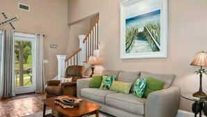 A living room with a sofa, a coffee table, a lamp, and a painting of a beach scene.