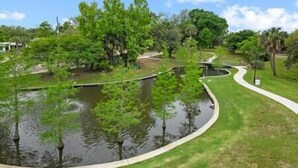 A landscaped area with a pond, curved pathways, and various trees.