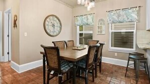A dining area with a wooden table and chairs, a wall clock, and windows with curtains.