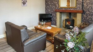 A living room with a sofa, a coffee table, a fireplace, and a television. - Bondcroft Farm Cottage (Eastby, near Skipton)
