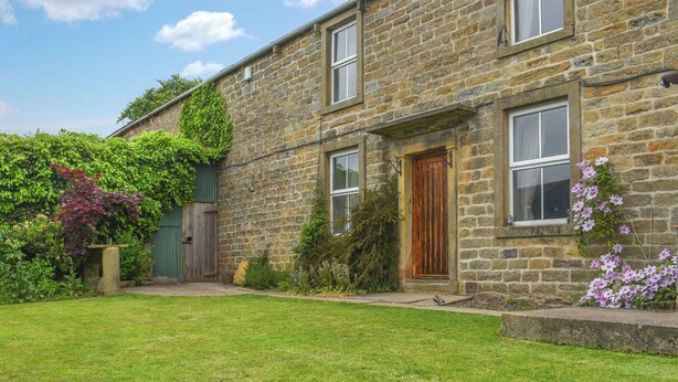 A stone house with a well-maintained lawn, a wooden door, and a window with a shutter. - Bondcroft Farm Cottage (Eastby, near Skipton)