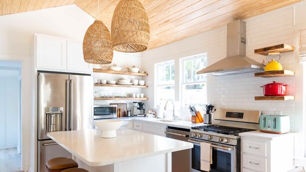 A modern kitchen with white cabinetry, stainless steel appliances, and a central island with stools. - Church St Collection - 106 (Fairhope)