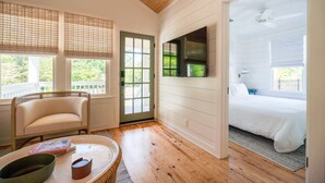 A room with a wooden ceiling, a bed with white bedding, a chair, a table with a bowl and a book, and a large window with blinds. - Church St Collection - 106 (Fairhope)