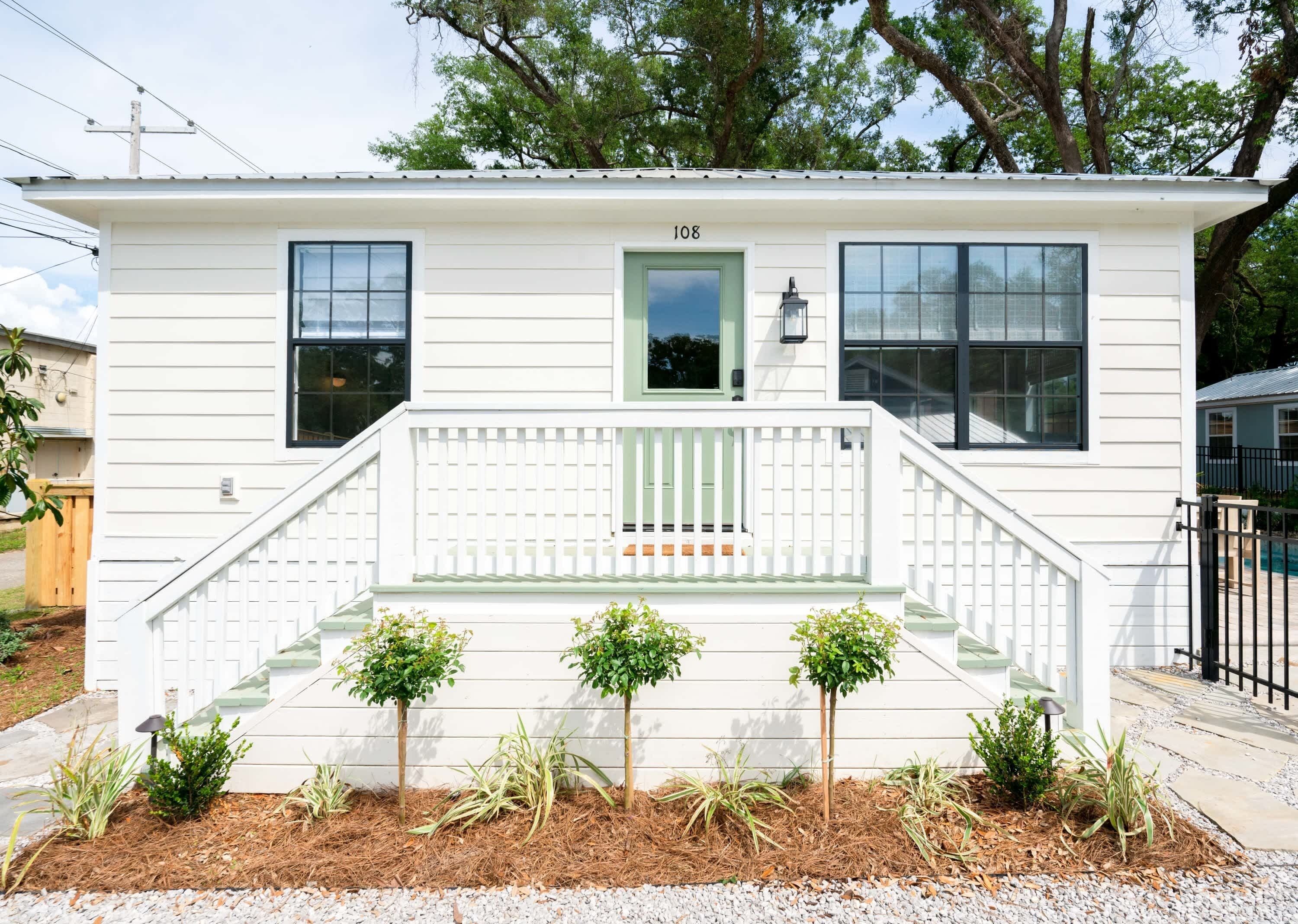 A single-story house with a front porch, a green door, and the number 108 on the wall.