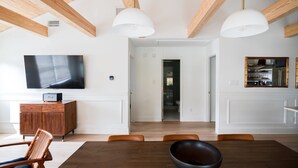 Ein modernes Wohnzimmer mit Holzboden, einem Flachbildfernseher, einer Holzkabine und einem Essbereich mit Tisch und Stühlen.