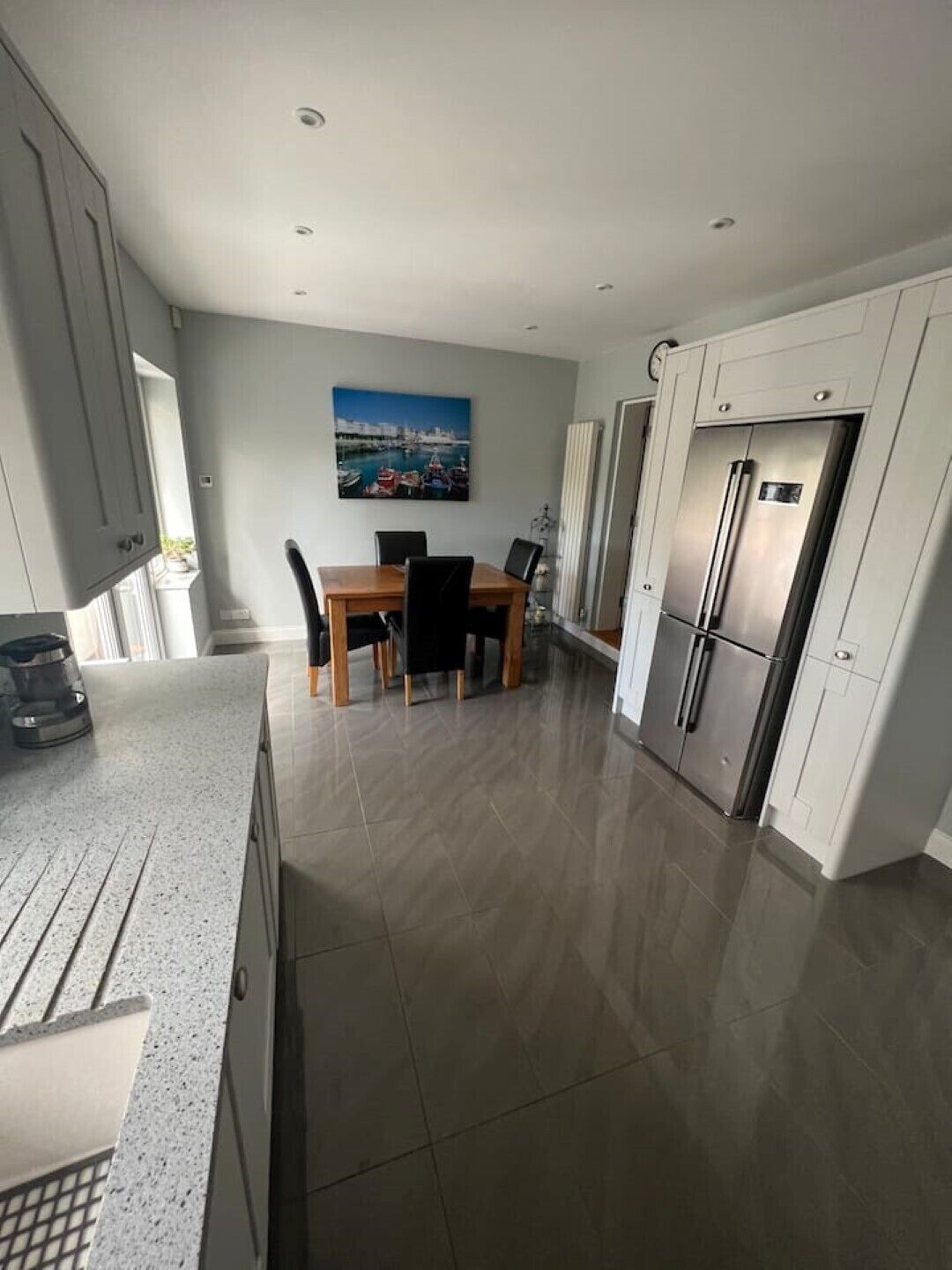 A modern kitchen with a dining area, featuring a stainless steel refrigerator, a dining table with chairs, and a cityscape painting on the wall.