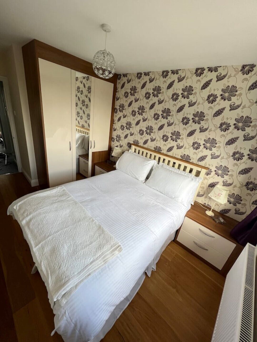 A neatly made bed with white linens, a wooden headboard, and a bedside table with a lamp.