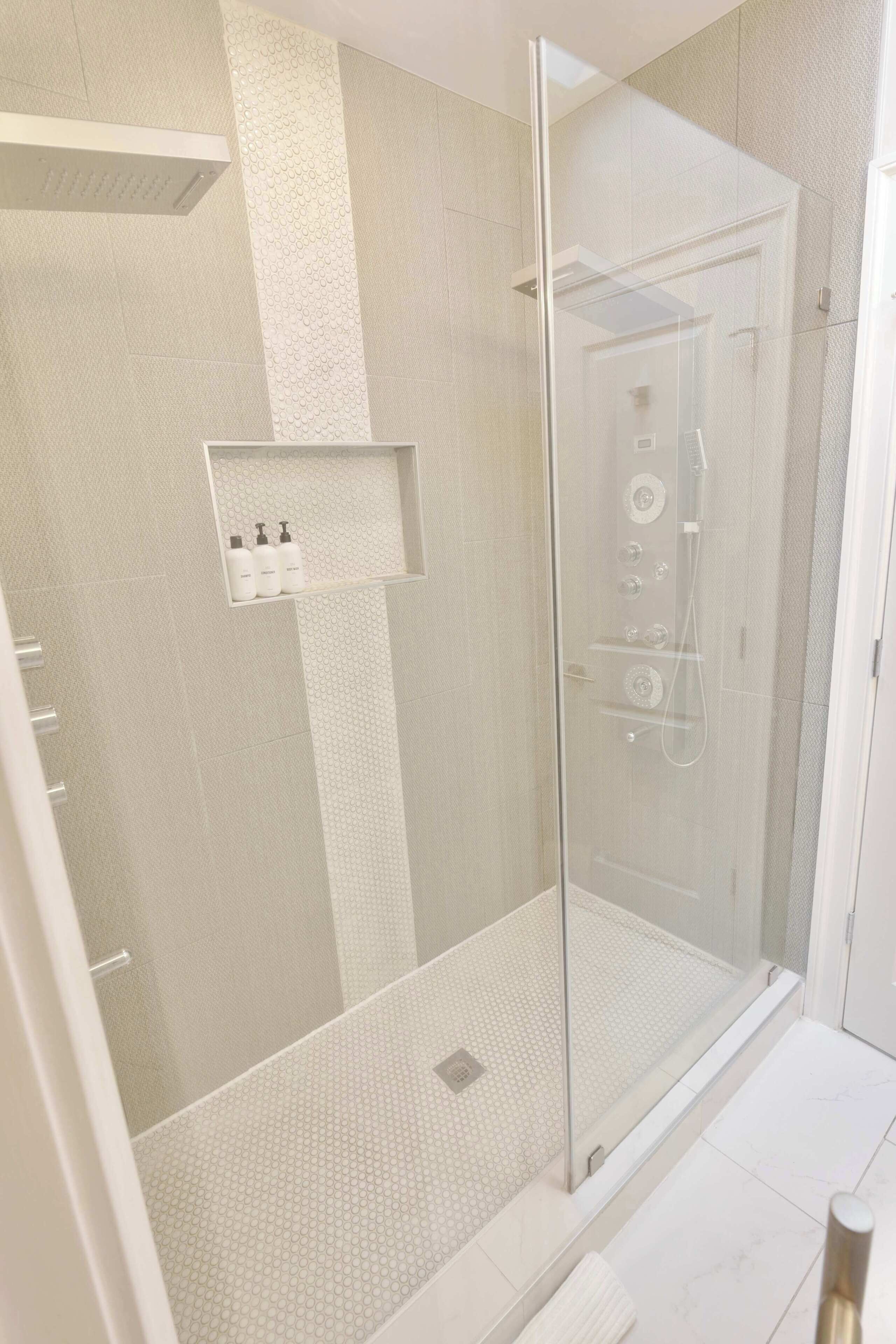 Een moderne douche met een glazen deur, een plankje met toiletartikelen en een betegelde vloer.