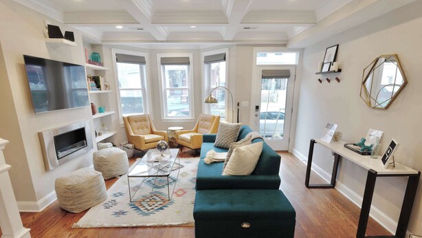 A living room with a green sofa, ottomans, a coffee table, and a TV mounted on the wall. - The Hip Strip - Stroll to Columbia Heights (Washington)