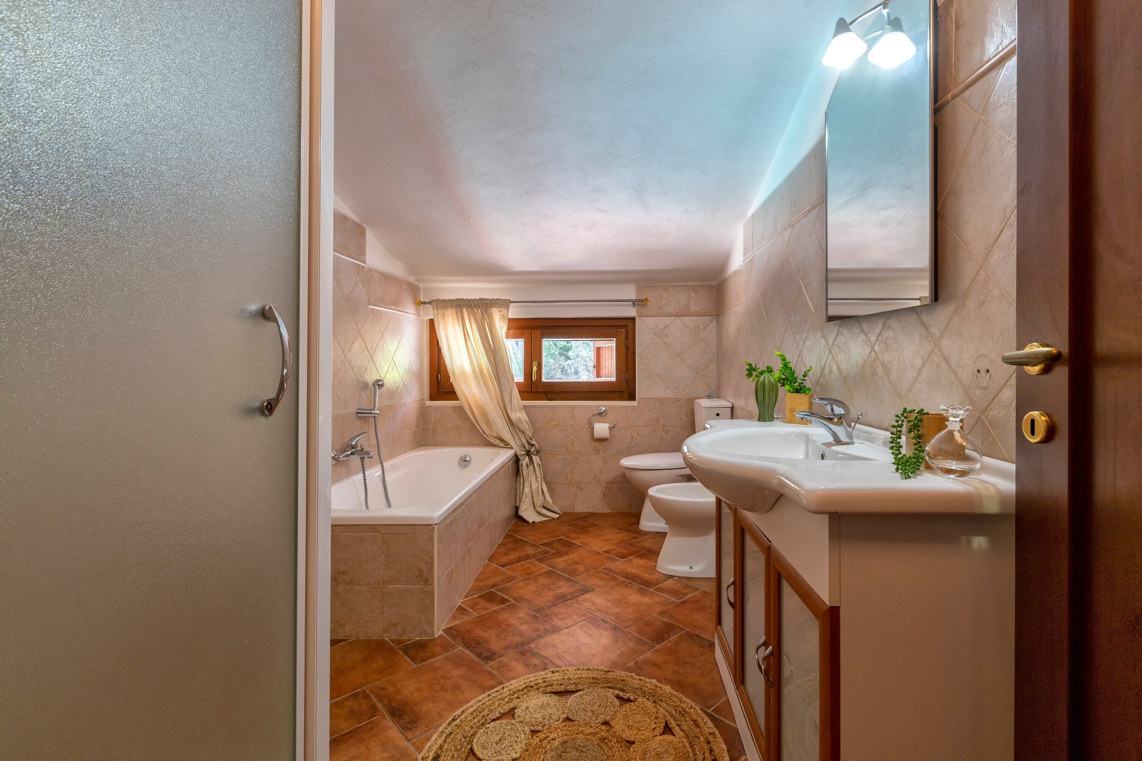 A bathroom with a bathtub, toilet, and sink, a window, and a mirror.