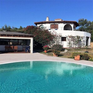 Une maison moderne dotée d’une piscine, d’un patio couvert et d’un jardin agrémenté de plantes à fleurs.