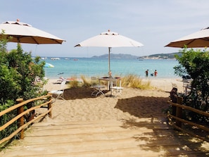 Een houten trap die naar een strand leidt, met parasols en stoelen.