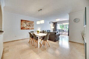 A spacious living area with a dining table, chairs, a sofa, and a large window.