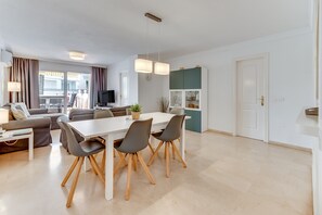 Un salon moderne comprenant un coin repas, un ensemble de canapés, un téléviseur à écran plat et une vue sur l’extérieur.