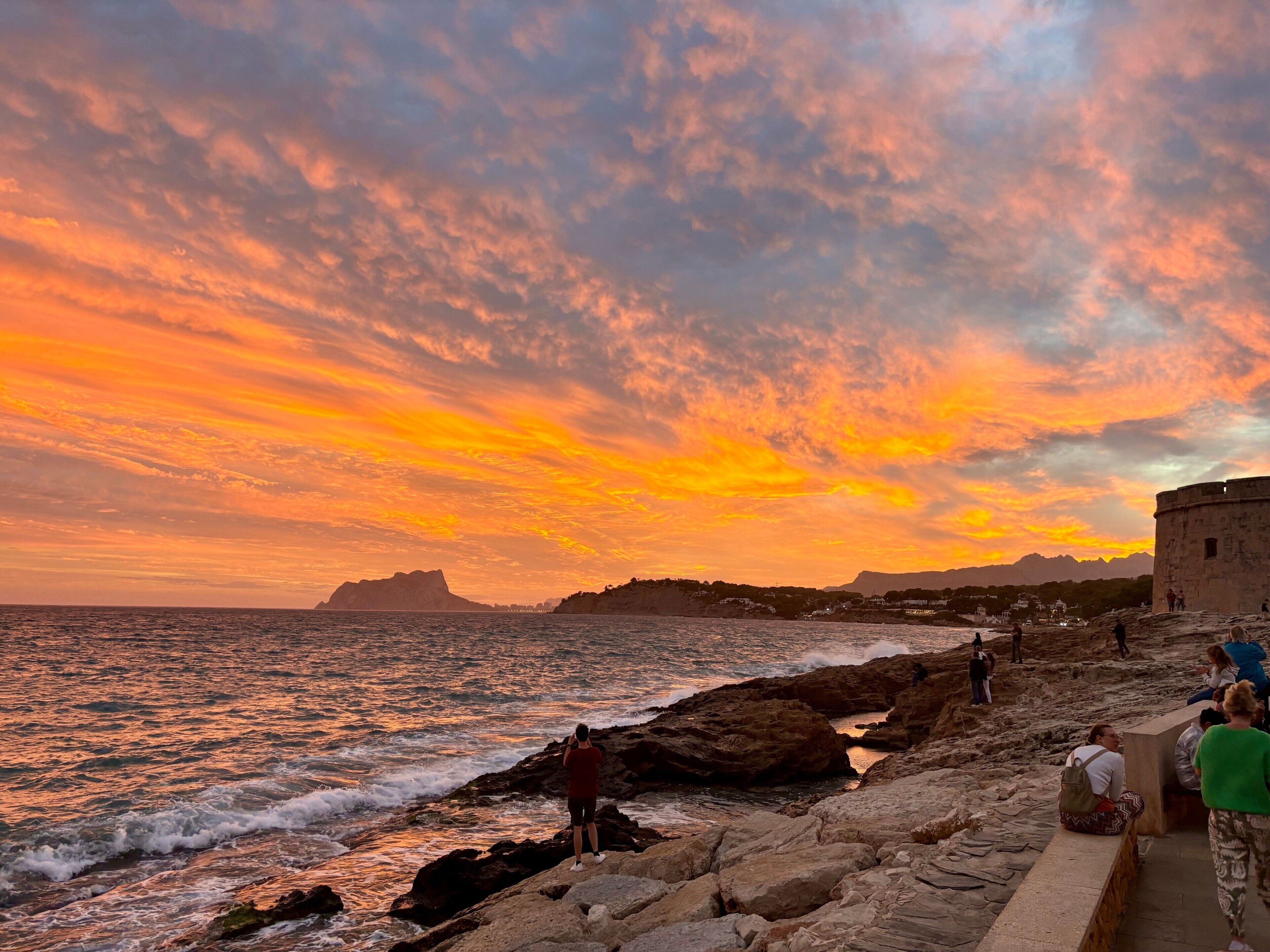 Un coucher de soleil sur la côte, avec un paysage rocheux et une structure en pierre.