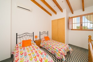 A bedroom with two beds, wooden beams, a window, and a wardrobe.