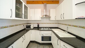 Een kleine keuken met witte kastjes, een gasfornuis, een oven en een spoelbak.